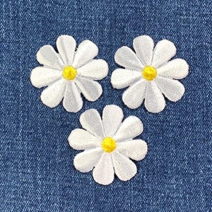 May include: Three white daisy flower patches with yellow centers on a blue denim background.