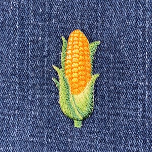 May include: An embroidered corn cob patch in yellow and green on a blue denim background.