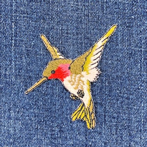 May include: Embroidered hummingbird patch with a red throat, yellow wings, and a long beak. The patch is on a blue denim background. The hummingbird is in flight, with its wings spread.
