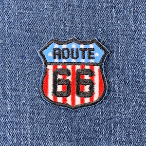 May include: An embroidered patch shaped like a highway sign with the text "ROUTE 66" in black, featuring red, white and blue colours.