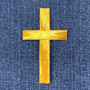 May include: A gold-colored cross patch on a blue denim background.