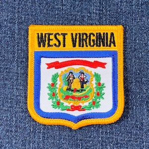 Könnte beinhalten: Gestickter Aufnäher mit den Worten "WEST VIRGINIA" in Gold über einem Schilddesign. Das Schild hat einen blauen Rand, ein weißes Innenteil mit einem Staatssiegel und ein rotes Band. Der Aufnäher hat einen goldenen Rand und ist auf einem blauen Jeanshintergrund angebracht.