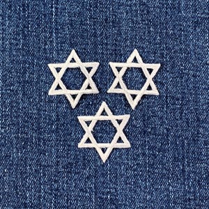 May include: Three white Star of David patches embroidered on a blue denim background. The patches are evenly spaced and feature a detailed, stitched design. The denim has a textured appearance.