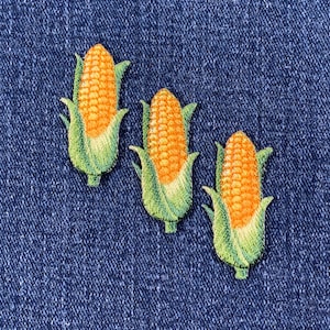 Peut inclure: Trois patchs brodés thermocollants représentant des épis de maïs avec des enveloppes vertes et des grains jaunes.