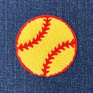 May include: A yellow softball patch with red stitching and a red border is centered on a blue denim background. The patch is round and has a textured appearance. The red stitching is in a classic softball pattern.