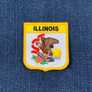 May include: Embroidered patch featuring the Illinois state seal. The patch has a yellow border and a white background. The seal includes a brown eagle, a shield, and the word "ILLINOIS" in black.
