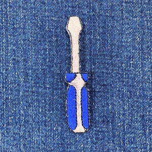 May include: A blue and white screwdriver patch on a blue denim background. The patch features a blue handle with white accents and a silver-colored blade. The patch is a simple, embroidered design.
