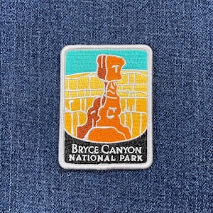 May include: Embroidered patch featuring a Bryce Canyon National Park design. The patch has a rectangular shape with a white border. The design includes a rock formation in shades of orange and brown, with a yellow and teal background. The text "BRYCE CANYON NATIONAL PARK" is displayed.