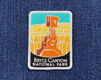 May include: Embroidered patch featuring a Bryce Canyon National Park design. The patch has a rectangular shape with a white border. The design includes a rock formation in shades of orange and brown, with a yellow and teal background. The text "BRYCE CANYON NATIONAL PARK" is displayed.