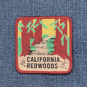 May include: A square patch featuring a scenic illustration of the California Redwoods. The design includes tall red trees, a path, and the text "CALIFORNIA REDWOODS" in a stylized font. The patch has a red border and is set against a blue denim background.