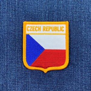 Könnte beinhalten: Gestickter Aufnäher mit der Flagge der Tschechischen Republik. Der Aufnäher hat ein weißes Rechteck mit dem Text "CZECH REPUBLIC" in Gold. Das Flaggen-Design umfasst ein blaues Dreieck, Weiß und Rot. Der Aufnäher hat einen goldenen Rand.