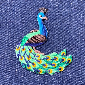 May include: Embroidered peacock patch in blue, green, and yellow. The patch depicts a detailed peacock with a blue head and neck, green body, and a fan of feathers in shades of green and yellow.