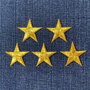 Peut inclure: Cinq écussons en forme d'étoiles dorées brodées sur un fond en denim bleu. Les étoiles sont espacées uniformément et ont un aspect texturé, ajoutant une touche d'élégance au design. Ces écussons sont parfaits pour décorer des vêtements ou des accessoires.