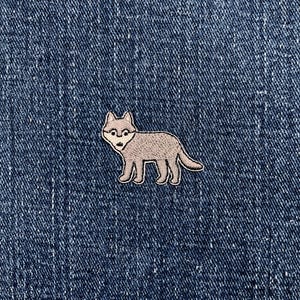Peut inclure: Un écusson de loup gris avec des lunettes, bordé de blanc, sur un fond en denim bleu. Le loup est debout, la tête légèrement tournée sur le côté. L'écusson est probablement thermocollant ou à coudre.