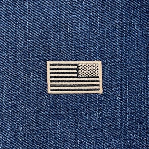 May include: A small, rectangular patch depicting the American flag. The patch is bordered in white and set against a dark blue denim background. The flag's stars and stripes are clearly visible, offering a patriotic design.