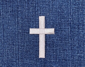 May include: A white cross emblem is set against a textured, dark blue denim background. The cross is made of a lighter fabric, creating a contrast against the denim. The image is a close-up, highlighting the details of the cross and the fabric.