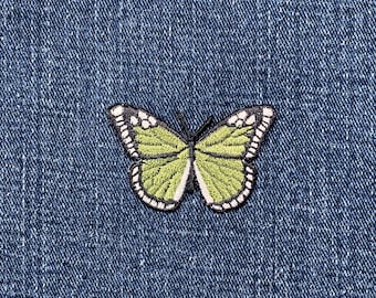 May include: A green and white butterfly patch with black detailing, set against a blue denim background. The patch has a white border and is embroidered.