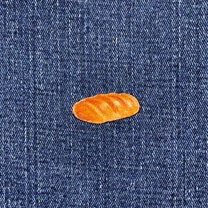 May include: A small, orange-brown bread loaf sticker on a blue denim background. The sticker has a detailed texture, with visible ridges and a slightly glossy finish. The denim has a classic, textured appearance.