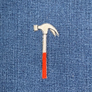 May include: Embroidered patch with a hammer design. The hammer head is off-white, the handle is white with a red base, set against a blue denim background. Ideal for customising clothing or accessories.