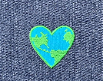 May include: A heart-shaped patch with a blue world map design and green continents, edged in green. The patch is set against a blue denim background, creating a striking contrast.