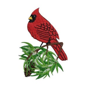 May include: An embroidered patch featuring a bright red cardinal bird with a black face mask and yellow beak, perched on a brown branch above a cluster of green pine needles and a small brown pinecone, all rendered in detailed thread work.