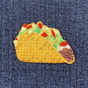 May include: Embroidered patch of a taco with a yellow shell, filled with red tomatoes, green lettuce, and brown meat. The patch is on a blue denim background. This patch is perfect for adding to clothing or accessories.