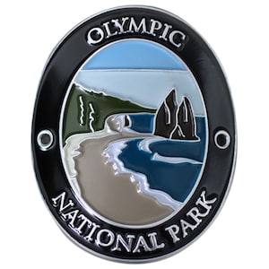 May include: A silver and black oval-shaped metal pin with a colorful image of a beach scene and the words "Olympic National Park".