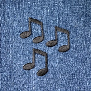 May include: Three black embroidered musical note patches on a blue denim background. The patches are evenly spaced and appear to be made of a textured fabric. The denim has a classic, faded appearance.