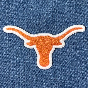 May include: Orange and white felt applique of a longhorn steer head. The steer head is on a blue denim background.