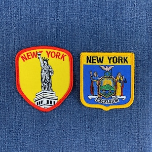 May include: Two embroidered patches featuring New York themes. The left patch is yellow with a red border, depicting the Statue of Liberty and the text NEW YORK. The right patch is blue and yellow, showing the New York state seal and text NEW YORK.