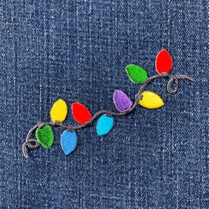 May include: A string of colourful Christmas lights embroidered on a blue denim fabric. The lights are red, yellow, green, purple, blue and orange.