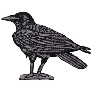 May include: Embroidered patch featuring a detailed black raven. The raven is depicted in profile, with intricate stitching defining its feathers, beak, and eye. The patch is designed to be ironed or sewn onto fabric, suitable for jackets, bags, or other apparel.