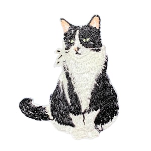 May include: An embroidered patch featuring a black and white cat sitting in a forward-facing position. The cat has a white chest, face, and paws, with black fur markings on its head, back, and tail. The design is rendered in detailed thread work.
