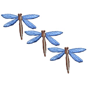 May include: Three embroidered dragonfly patches. Each dragonfly has blue wings and a brown body. The wings are detailed with stitched lines, and the bodies have a textured appearance. The patches are set against a white background.