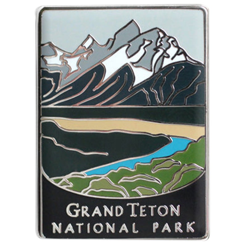 May include: A rectangular pin depicting the Grand Teton National Park. The design shows mountains, a lake, and a river, with the text "Grand Teton National Park" at the bottom. The pin has a silver border.