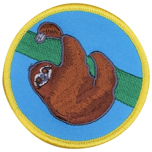 May include: A circular embroidered patch featuring a brown sloth hanging from a green branch against a bright blue background. The patch is finished with a thick, vibrant yellow stitched border that frames the entire circular design.