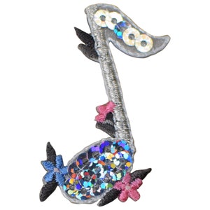 May include: A silver musical note with sequins and black and pink embroidered flowers. The note is decorated with iridescent sequins.