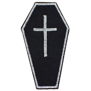May include: A coffin-shaped embroidered patch featuring a black fabric base with a white stitched border. Centered on the patch is a white embroidered cross. The design is flat and symmetrical, showcasing clean lines and detailed thread work throughout.