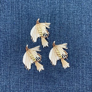 May include: Three embroidered patches of brown and white fishing flies on a blue denim background.