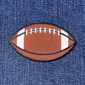 May include: A brown football patch with white stripes and stitching, outlined in black. The patch is an oval shape and is set against a blue denim background.