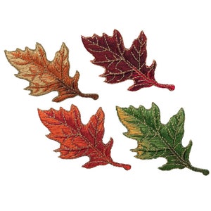 May include: Four embroidered oak leaves in autumnal colours: orange, red, burgundy, and green. Each leaf has detailed stitching and gold thread accents, creating a textured, decorative effect. The leaves are arranged against a white background.