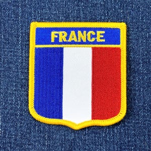 May include: Embroidered patch featuring the French flag design. The patch has a blue top section with the word "FRANCE" in yellow letters. The main section displays vertical stripes of blue, white, and red, outlined with a yellow border.