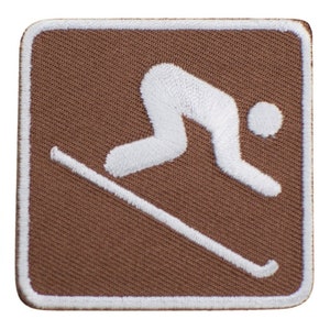 May include: Brown fabric patch with a white embroidered skier silhouette. The skier is in a downhill position with skis and ski poles.