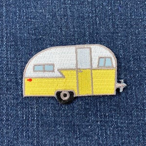 May include: Embroidered patch of a vintage camper, featuring a yellow and white colour scheme. The camper has a single door and a window on each side.