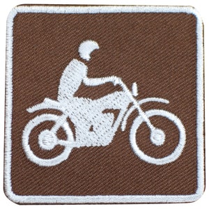 May include: White embroidered motorcycle patch on a brown background.