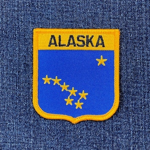 May include: A rectangular patch with a yellow border and the word "ALASKA" in black letters at the top. The patch has a blue background with yellow stars, including the Big Dipper constellation.