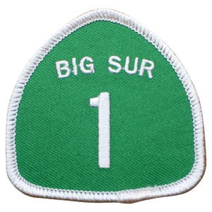 May include: A shield-shaped embroidered patch with a green background and a white border. The text BIG SUR is stitched in white at the top, and a large white number 1 is centered below the text. The patch features a clean, stitched edge finish.