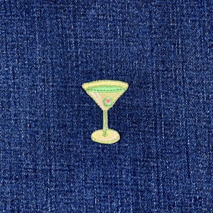 May include: Embroidered patch of a martini glass with a yellow outline, a light green interior, and a pink olive. The patch is set against a dark blue denim background.