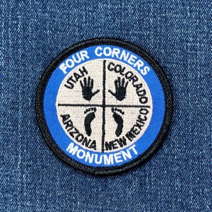 May include: A circular patch with a blue border and black trim. The patch features the words "FOUR CORNERS MONUMENT" and the names of four states: Utah, Colorado, Arizona, and New Mexico. The design includes handprints and footprints.