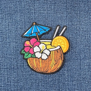 May include: An embroidered patch featuring a coconut drink with a blue cocktail umbrella, two straws, and a slice of orange. The coconut is decorated with a bright pink hibiscus flower and a white hibiscus flower with green leaves.